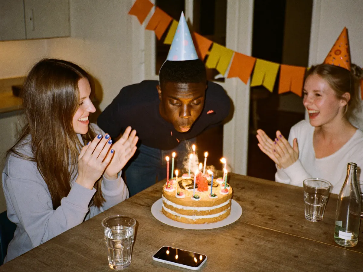 Venner feirer bursdag rundt et kjøkkenbord med kake og lys