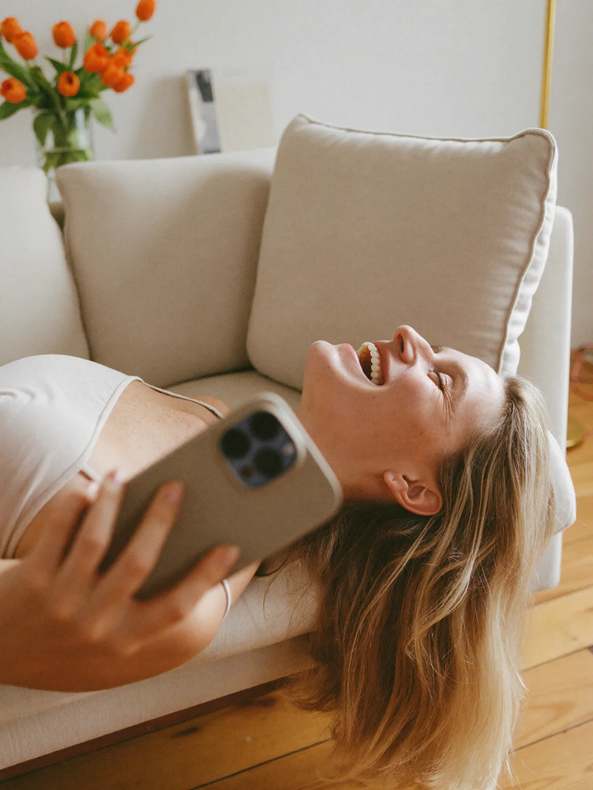 Kvinne ler mens hun åpner en gave på mobilen i en lys stue